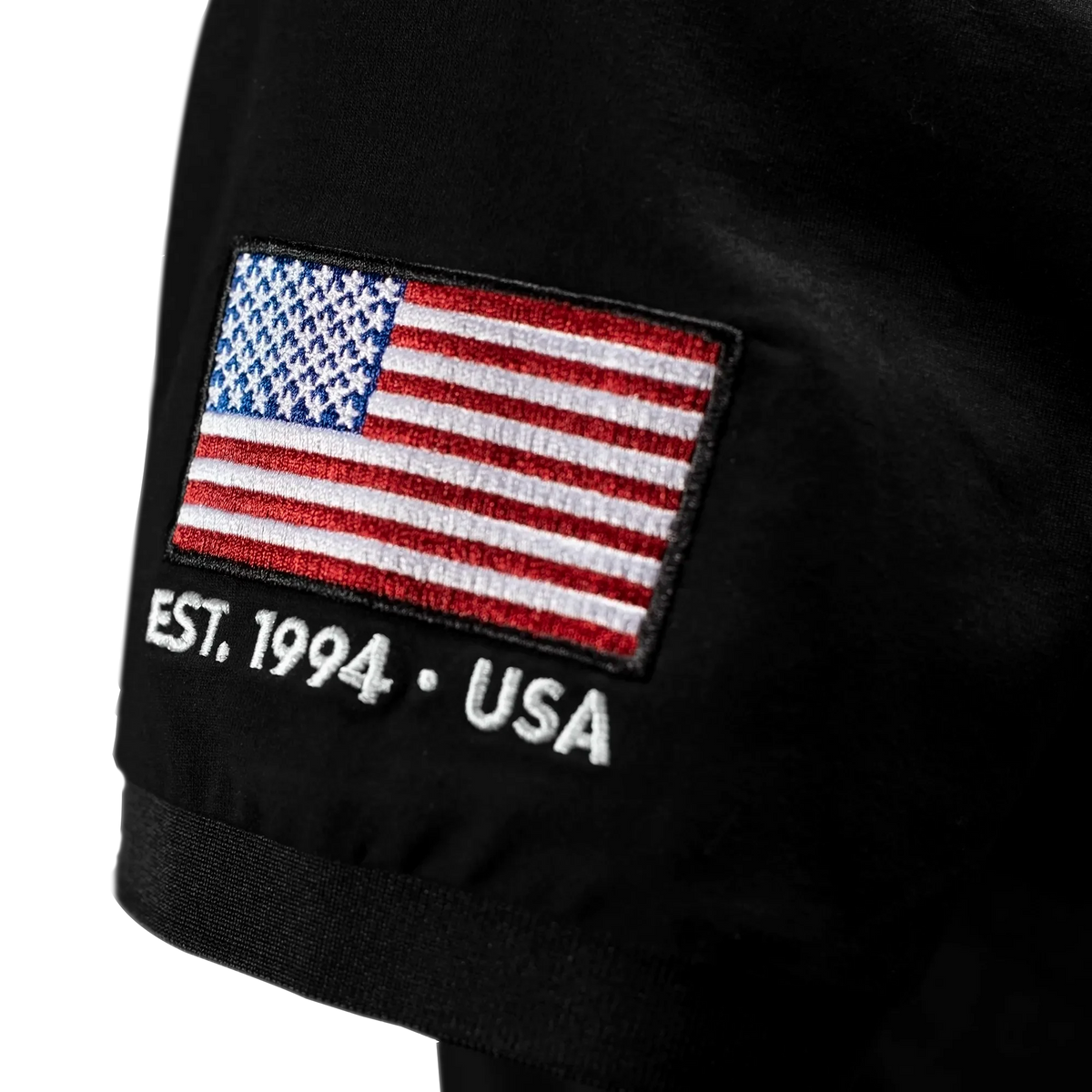Black polo shirt with American flag patch and 'EST. 1994 • USA' text.