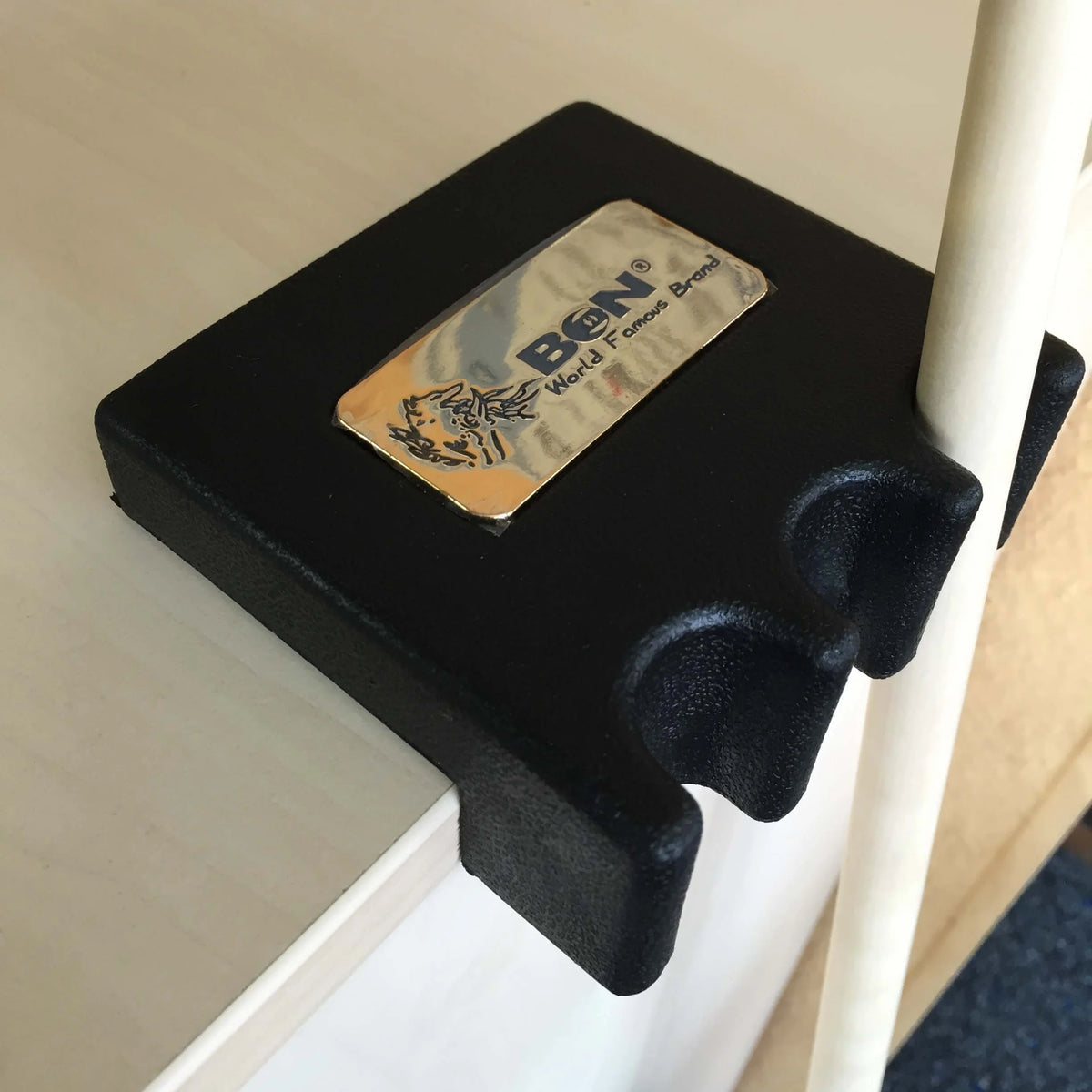 BCN Two-Slot Table-Edge Cue Holder In Black With A Gold BCN Badge, Clamped To A Table Edge And Holding A Cue